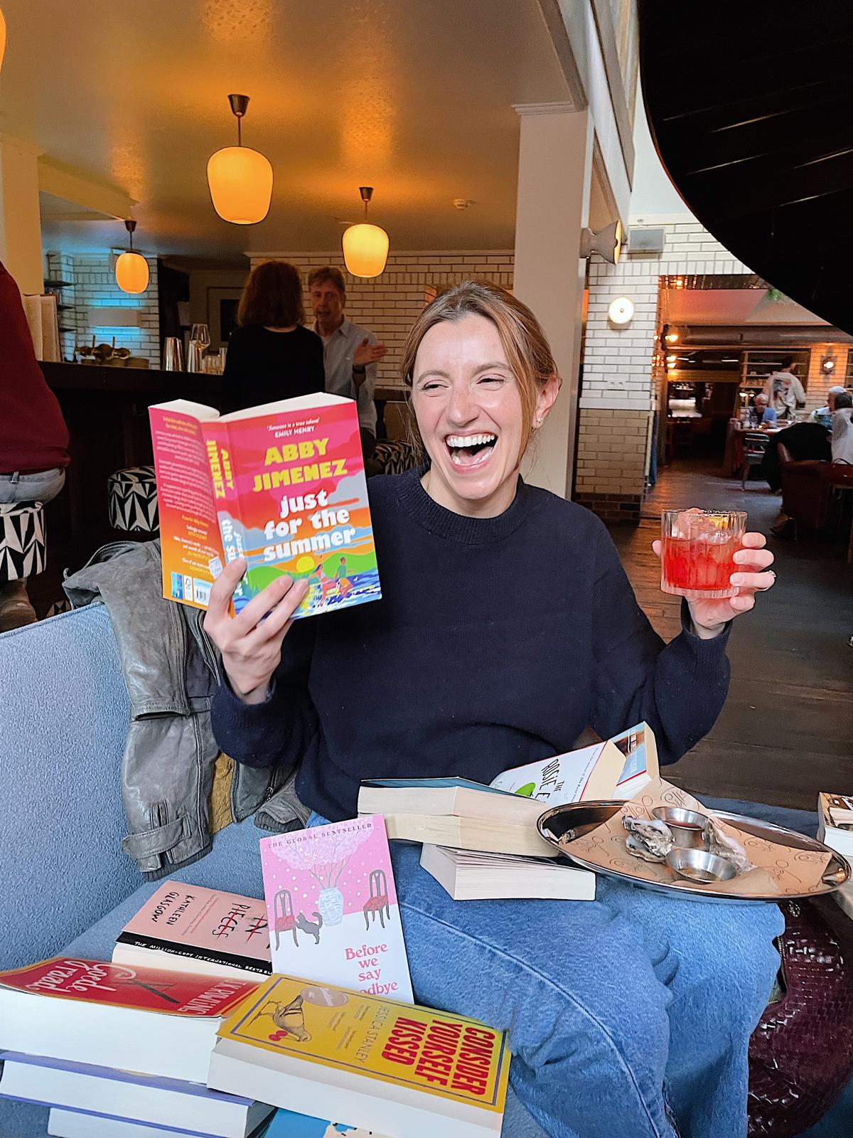Emily at a book event, laughing with lots of books around her